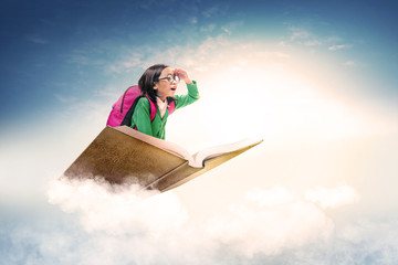 Asian cute girl with glasses and backpack sitting on the book with blue sky background