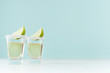 Golden mexican tequila shot drinks with salty rim, piece lime in elegant glass on pastel green wall, white wood table, copy space.