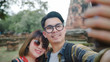 © tirachard - Traveler Asian couple using smartphone taking selfie while spending holiday trip at Ayutthaya, Thailand, Couple enjoy their journey at amazing landmark in traditional city.