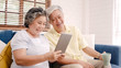 © tirachard - Asian elderly couple using tablet and drinking coffee in living room at home, couple enjoy love moment while lying on sofa when relaxed at home. Enjoying time lifestyle senior family at home concept.