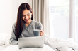 © Art_Photo - Young woman relaxing and drinking cup of hot coffee or tea using laptop computer on a cold winter day in the bedroom.woman checking social apps and working.Communication and technology concept