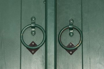 Old green door with  aged metal door handle in the form of ring.