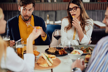 Poster - Multiethnic friends sitting at restaurant, drinking alcohol, chatting and having burgers for dinner.