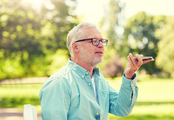 Poster - technology, senior people, lifestyle and communication concept - close up of happy old man using voice command recorder or calling on smartphone at summer park