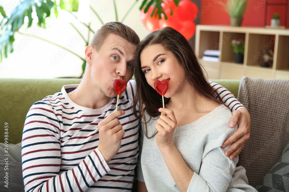 Happy young couple with heart shaped lollipops at home