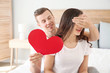 © Pixel-Shot - Young man with paper heart covering eyes of his wife at home