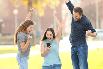 Wall Mural - Three excited friends jumping checking smart phone in a park