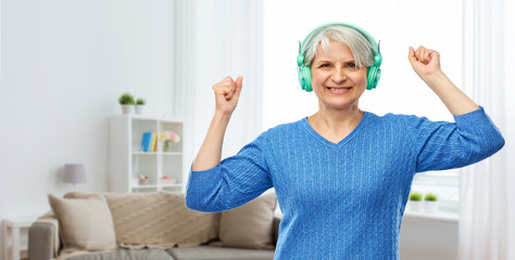 Canvas Print - technology and old people concept - smiling senior woman in glasses and headphones listening to music over home living room background