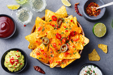 Nachos chips with melted cheese and dips variety in black bowl. Top view.