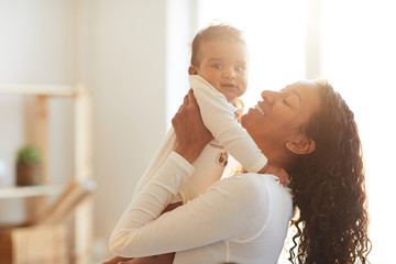 positive loving attractive young african mother with curly hair standing in living room and picking 