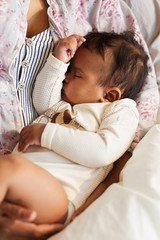 close-up of unrecognizable mother in cotton shirt holding sleepy black baby boy in arms