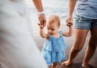 Canvas Print - A midsection of parents with toddler daughter walking on beach on summer holiday.