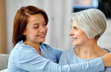 family, generation and people concept - happy smiling senior mother with adult daughter hugging at home