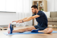 Sport, Fitness And Healthy Lifestyle Concept - Man Stretching Leg On Exercise Mat At Home
