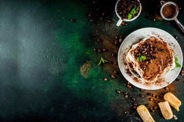 Homemade italian dessert tiramisu on plate, with cocoa and coffee beans, decorated with mint, dark green background copy space