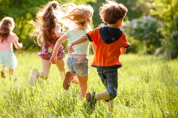 a group of children playing and running in the park on a green gozon.