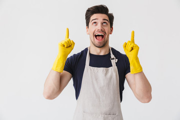 Canvas Print - Photo of caucasian young man wearing yellow rubber gloves for hands protection pointing fingers at copyspace while cleaning house