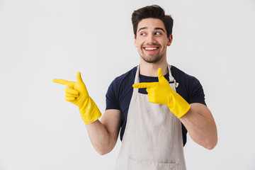 Wall Mural - Photo of optimistic young man wearing yellow rubber gloves for hands protection pointing fingers at copyspace while cleaning house