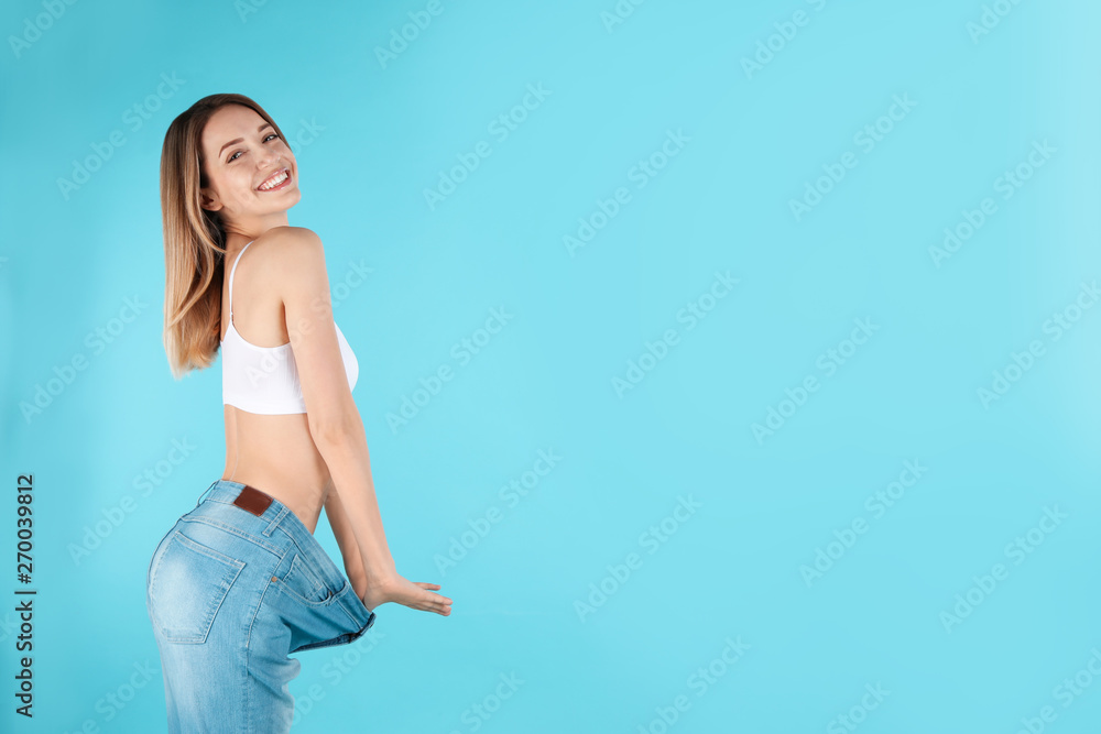 Slim woman in oversized jeans on color background, space for text. Perfect body - obrazy, fototapety, plakaty 