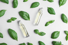 Glass Bottles With Essential Oil Among Basil Leaves On Light Background, Flat Lay