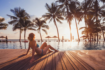 Wall Mural - tropical getaway retreat in luxury beach hotel, luxury travel, woman relaxing near swimming pool at sunset