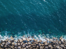 Ocean Water Surface Texture View From Above, Background Pattern Of Blue Sea And Cube Stones On Coastline