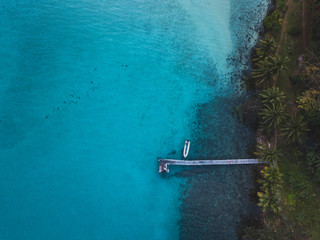 Wall Mural - aerial landscape of tropical island and wooden pier with boat, top down view of blue water and palm trees from drone