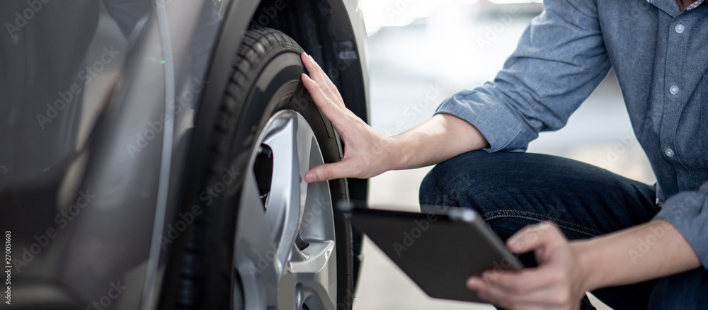 Asian auto mechanic holding digital tablet checking car wheel in auto service garage. Mechanical maintenance engineer working in automotive industry. Automobile servicing and repair concept - obrazy, fototapety, plakaty 