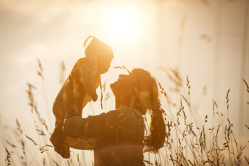 Happy child and his mom have fun outdoors in a field flooded with sunlight