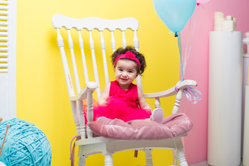 Happy smiling sweet baby girl sitting on armchair with birthday balloons