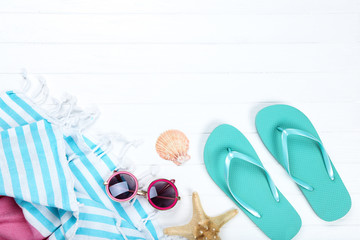 Wall Mural - Pair of flip flops with seashells, towel and sunglasses on white wooden table