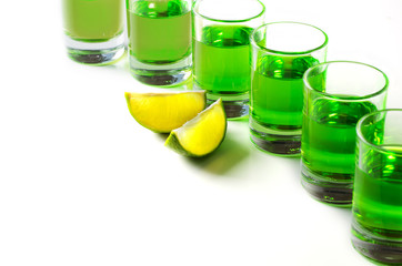  Absinthe green liquor in glasses. Alcoholic hallucinogenic beverage. White background. Pieces of lime. Copy space