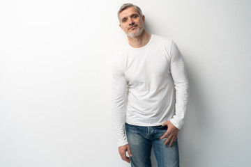 Cheerful man of middle age against white background, wearing jeans and white T-shirt, mid shot.