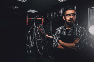 Wall Mural - Handsome bearded man in glasses is standing near fixed bicycle at his own workshop.