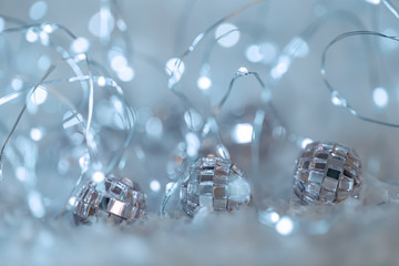 Wall Mural - Small decorative balls with a mirror and a luminous garland on a snow. Blurred festive gray background with white bokeh.