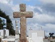 © Liliana Akstein - Scene in a cemetery: close-up of a religious stone cross. In the background, tombs, crosses and a cloudy sky. Sadness and faith.