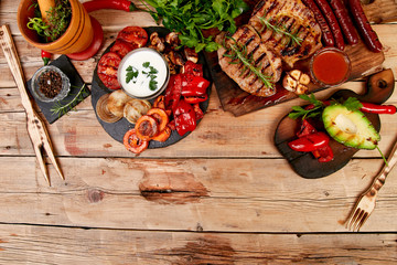 Wall Mural - Grilled meat. Steak pork grill on wooden cutting board with a variety of grilled vegetables on  rustic background  Top view. Flat lay. Copy space.