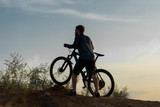 Fototapeta  - Cyclist in shorts and jersey on a modern carbon hardtail bike with an air suspension fork rides off-road on the orange-red hills at sunset evening in summer