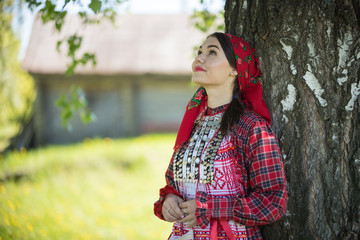 Wall Mural - Young woman in traditional russian clothes standing under a tree and looking up