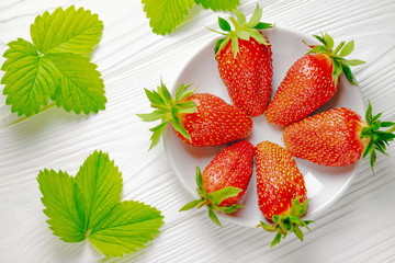 Wall Mural - Top view strawberries in a white plate on a white wooden table and strawberry leaves