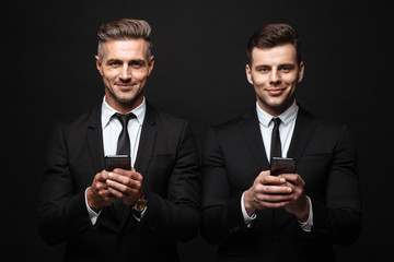 Wall Mural - adult business men posing isolated over black wall background using mobile phones.