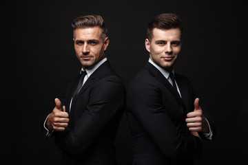 handsome two adult business men posing isolated over black wall background.