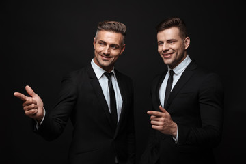 handsome two adult business men posing isolated over black wall background.