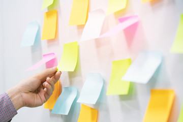 close up hand people business man  notes pad in the wall at meeting room. Sticky post it note paper reminder schedule board. Colorful variety copy empty space. soft focus.