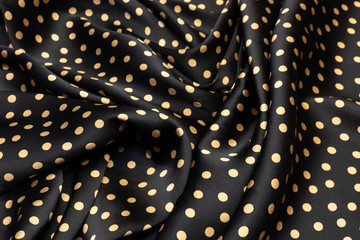 Satin silk fabric with beige peas on black in artistic layout. Texture, background, pattern.
