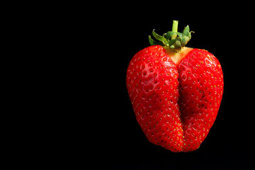 Close up of a funny shaped, ripe and juicy strawberry fruit, looking like a female butt, on a black background