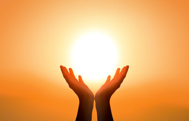 free concept: raised hands catching sun on sunset sky