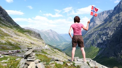 Sticker - Happy tourist woman holds norwegian flag, enjoying nature landscape from Trollstigen viewpoint area. Trolls Path mountain road in Norway. Touristic attraction