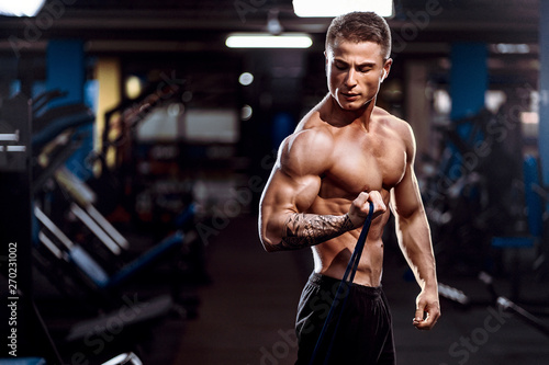 Fototapeta  Hard working well built sportsman exercising with a resistance band in gym