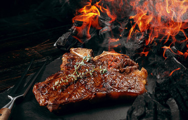 barbeque steak on a black slate board with meat fork and grill coals next to it